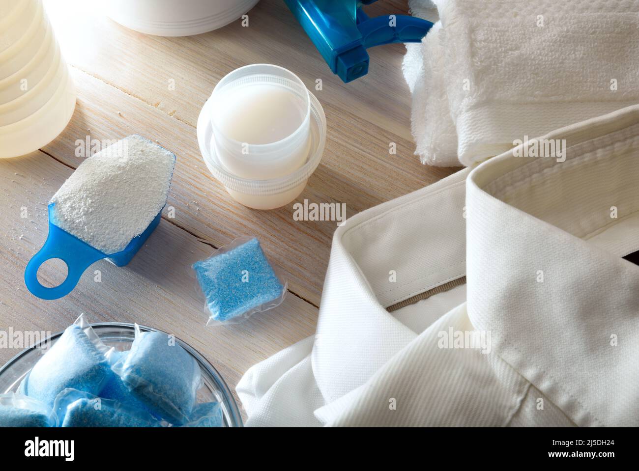 Dettaglio di vari tipi di prodotti chimici per il lavaggio di abiti su tavola di legno e vestiti bianchi intorno. Vista dall'alto. Composizione orizzontale. Foto Stock