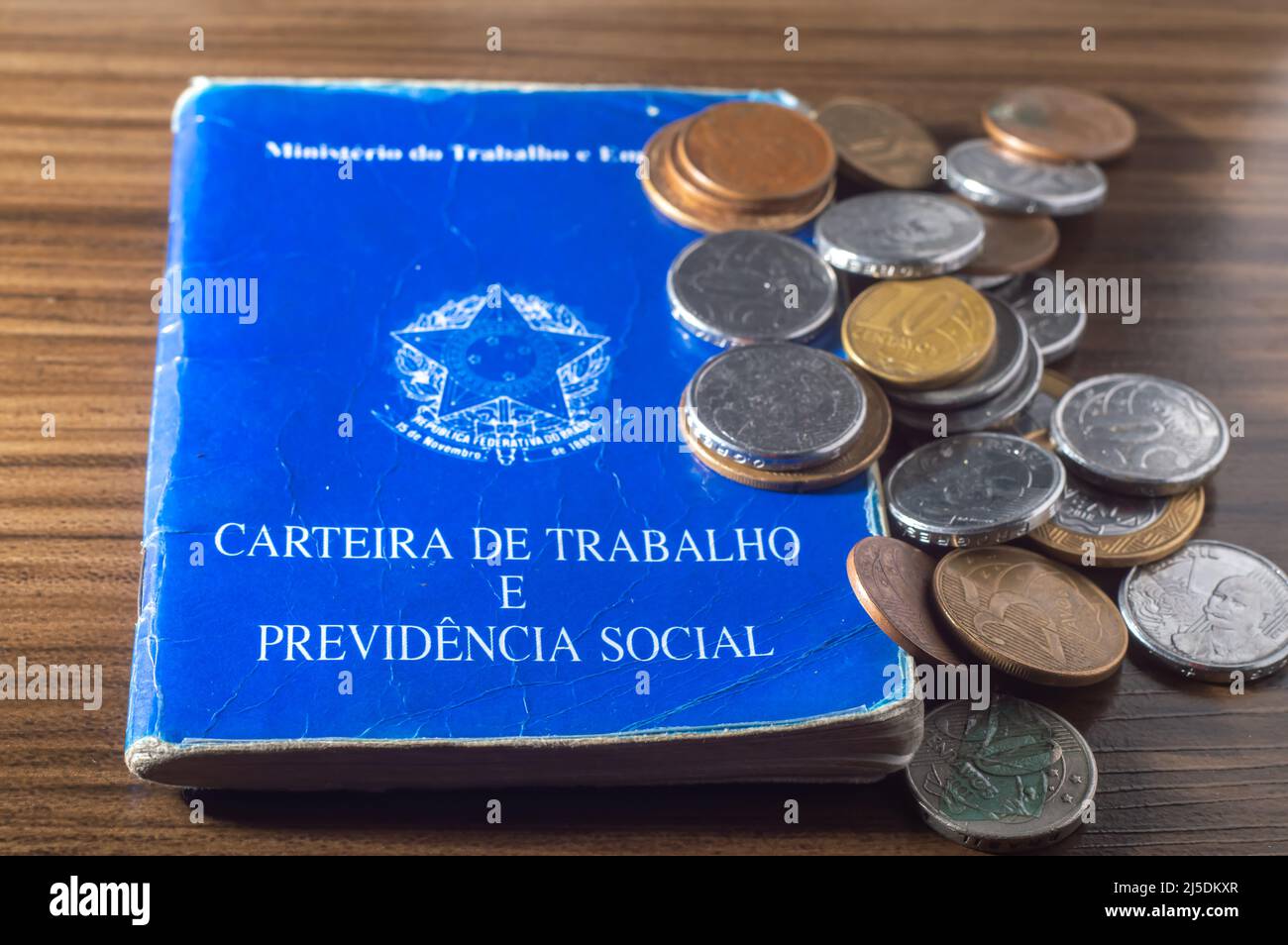 Traduzione: Repubblica Federativa del Brasile, Ministero del lavoro. Scheda di lavoro (Carteira de trabalho) accanto alle monete reali brasiliane, denaro brasiliano. Foto Stock