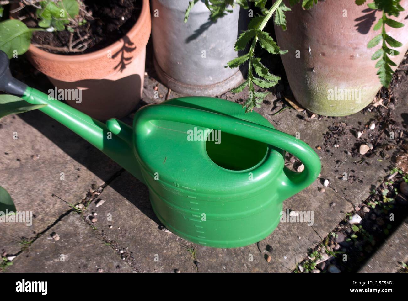 Annaffiatura plastica verde può vicino a piantatrici e vaso di fiori in giardino a Ruskington, Sleaford, Inghilterra, Regno Unito Foto Stock