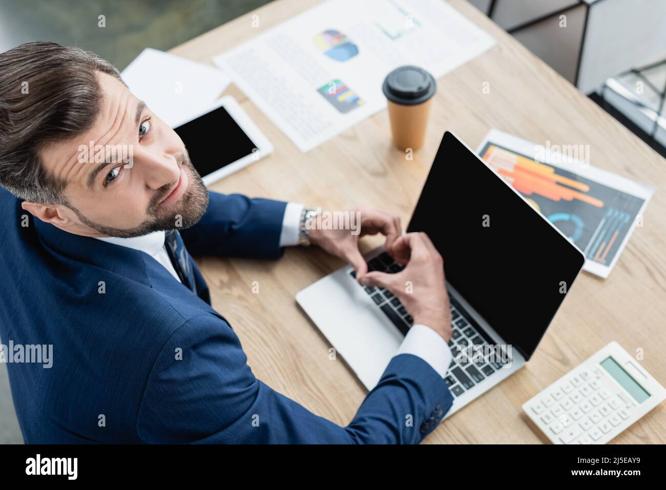 vista dall'alto di un economista felice che mostra un cartello cardiaco vicino a un computer portatile con schermo vuoto Foto Stock