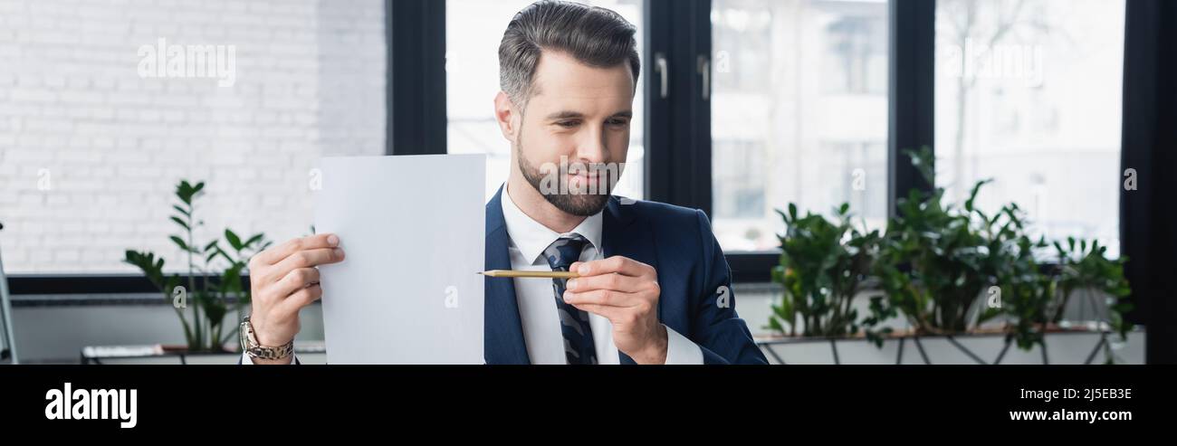 uomo d'affari brunette che punta con la matita a carta bianca, banner Foto Stock