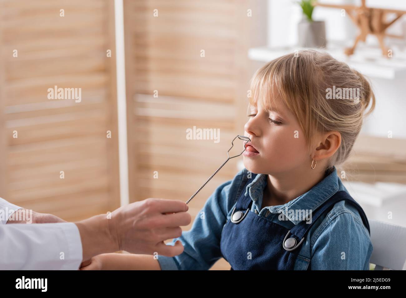 Terapista di discorso in cappotto bianco che tiene lo strumento vicino al bambino in aula Foto Stock