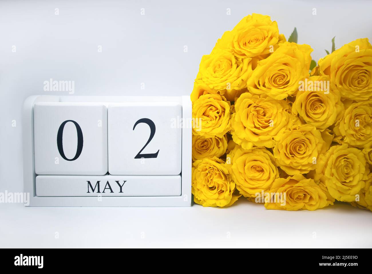 Maggio 2 su un calendario bianco in legno e un bouquet giallo di rose si trovano fianco a fianco Foto Stock