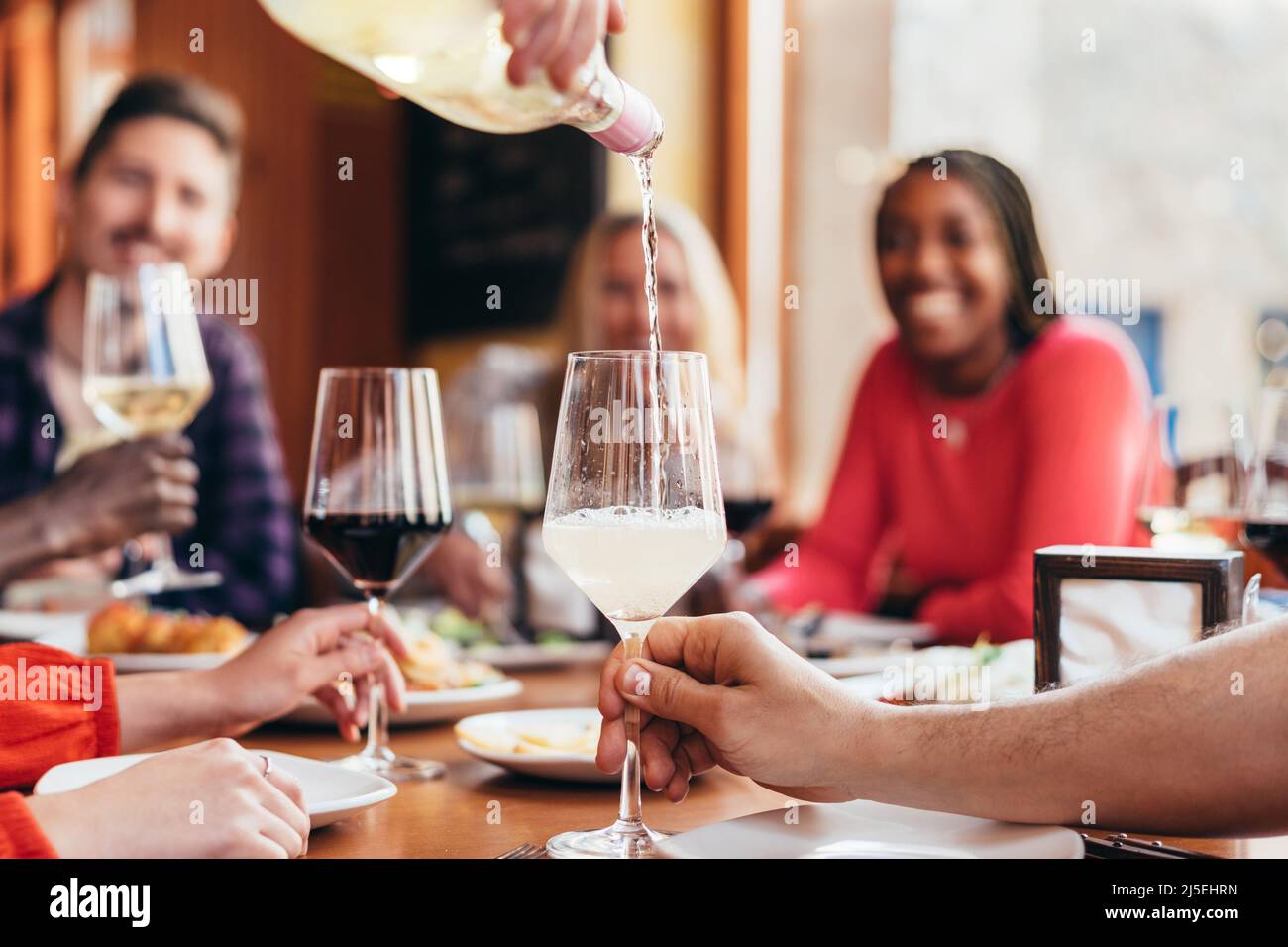 il cameriere versa il vino bianco in un bicchiere con molti commensali Foto Stock