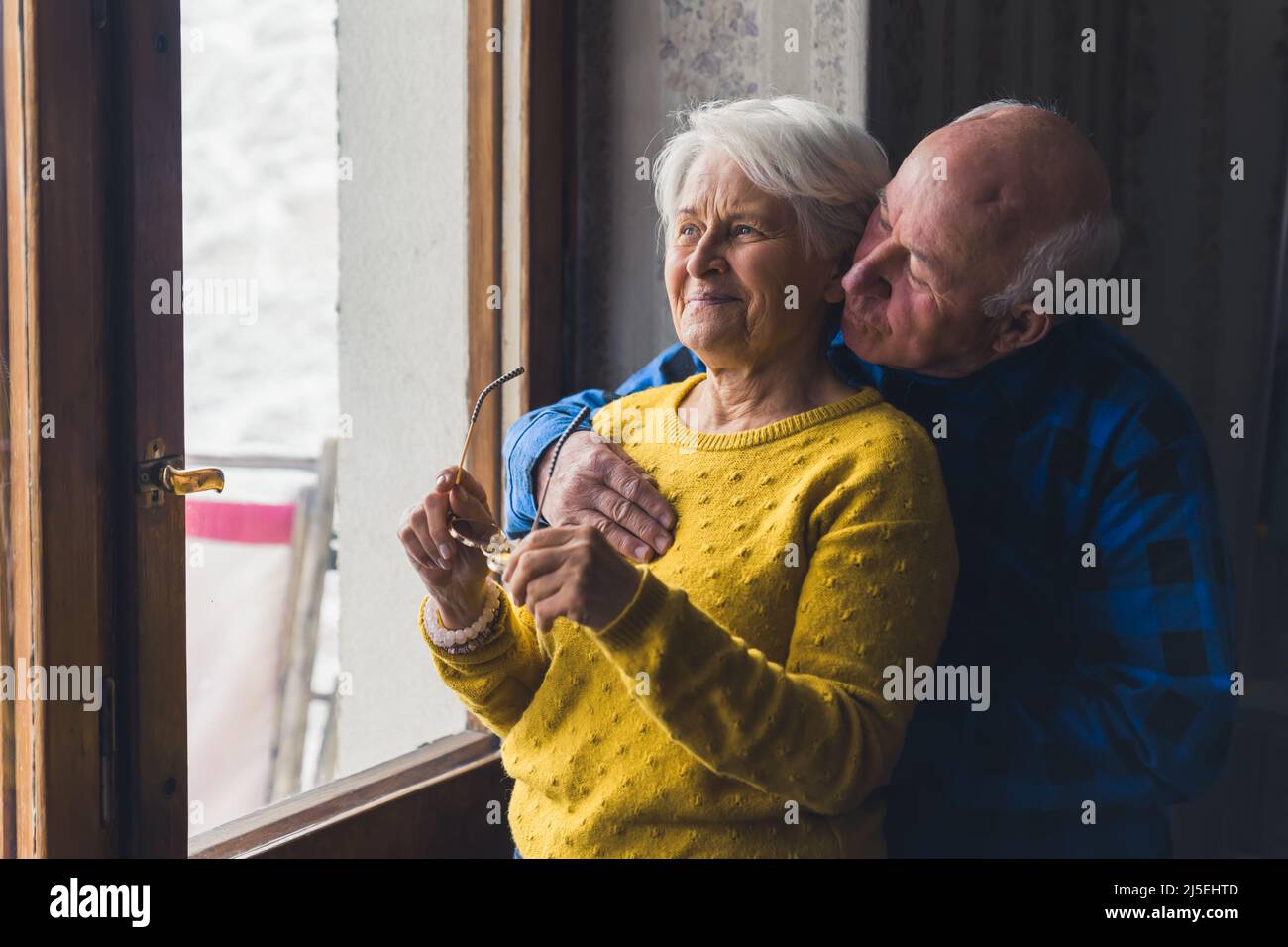 uomo anziano che abbraccia la donna anziana vicino alla finestra persone anziane sostengono concetto di camera al coperto medio colpo . Foto di alta qualità Foto Stock