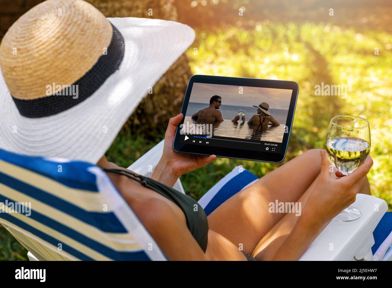 donna che guarda un film romantico sul servizio di streaming multimediale mentre si rilassa in poltrona da giardino Foto Stock