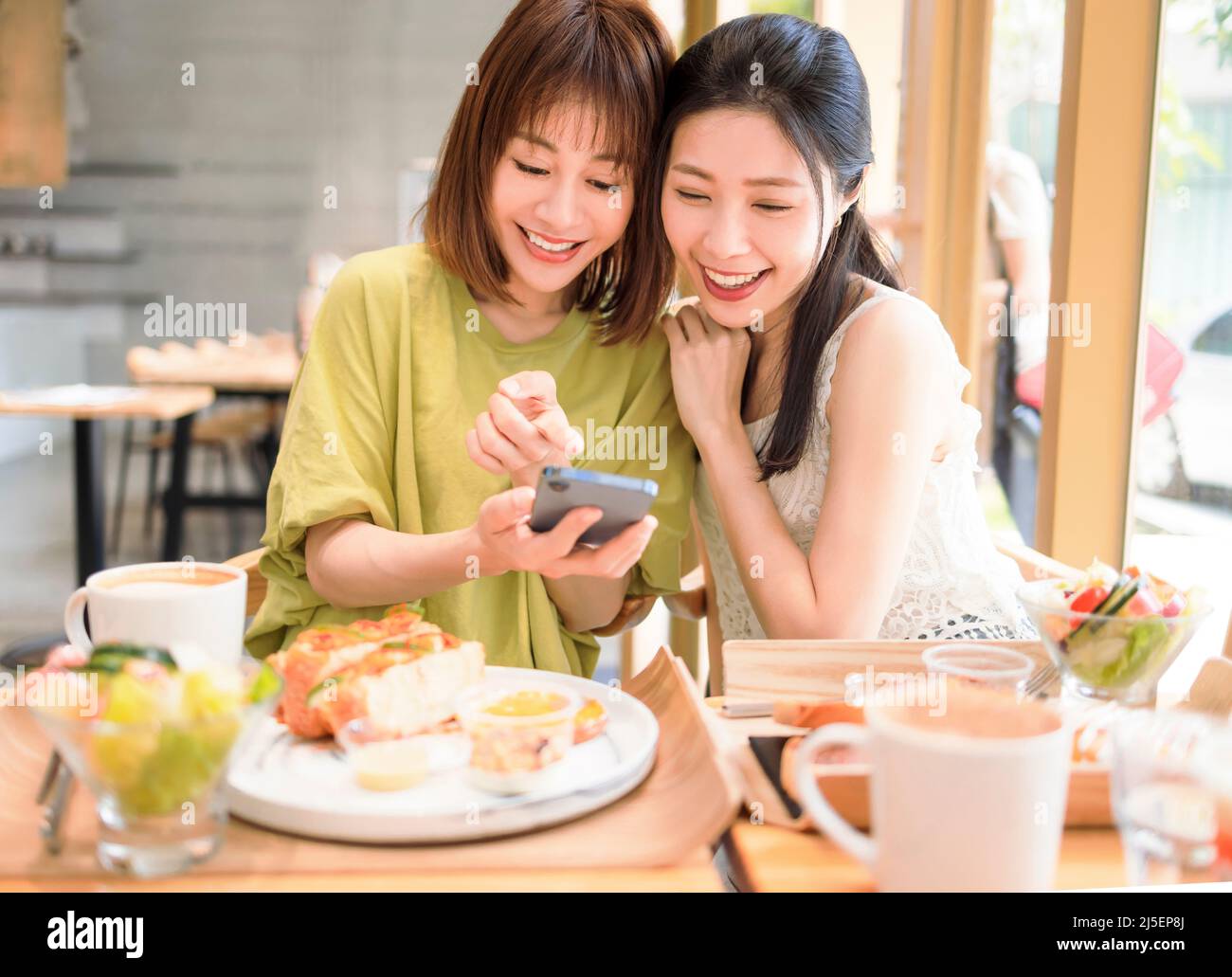 Giovani donne seduti al ristorante guardando il telefono cellulare e sorridenti Foto Stock