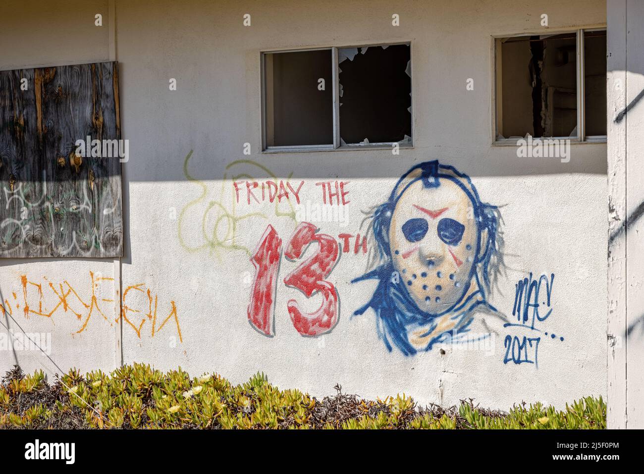 Graffiti creepy che mostrano il decadimento urbano su una casa abbandonata Foto Stock