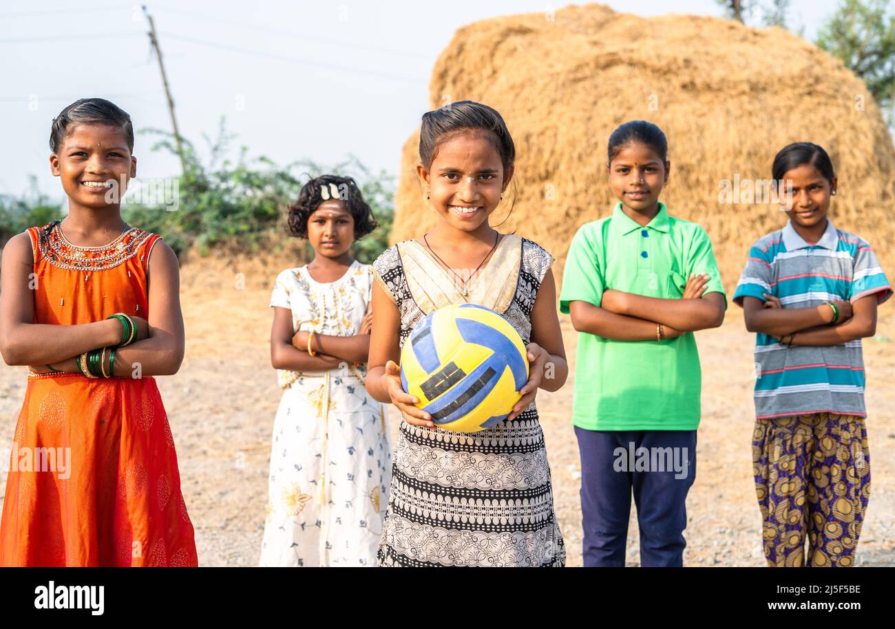 Gruppo di ragazze del villaggio indiano con un bambino che tiene il calcio guardando la macchina fotografica durante l'addestramento - concetto di emozione positiva, addestramento e hobby Foto Stock