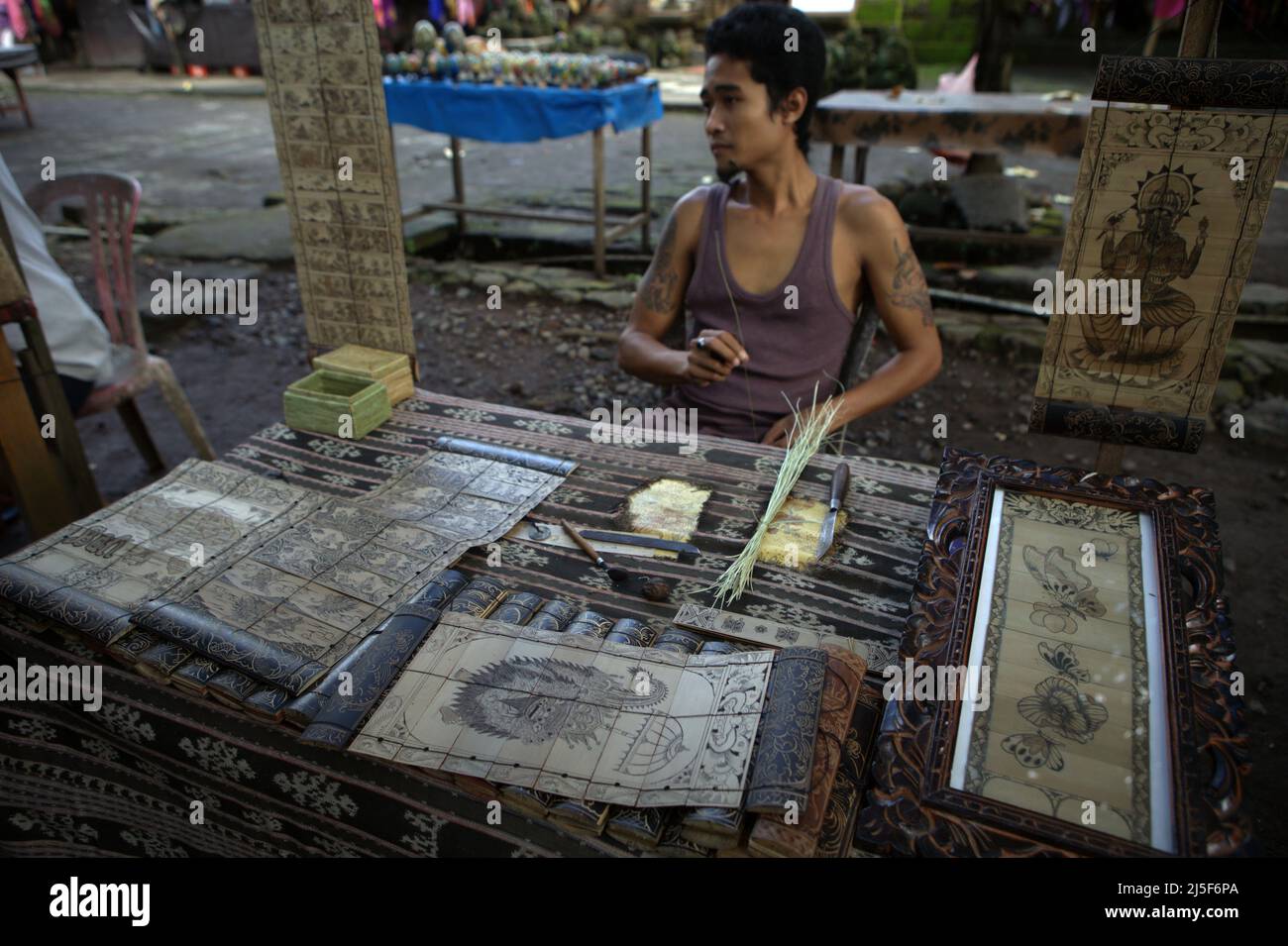 Un artista in attesa di clienti al suo stand di arti di foglie di palma nel villaggio tradizionale di Tenganan Pegringsingan a Karangasem, Bali, Indonesia. Foto Stock