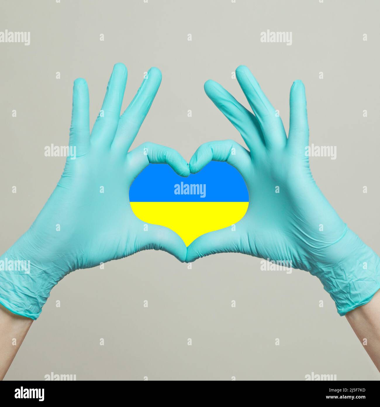 Cuore con bandiera Ucraina dalle mani in guanti medico blu su sfondo grigio Foto Stock