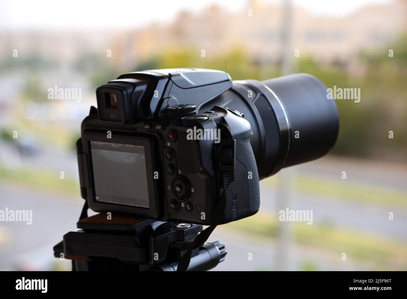 Una fotocamera digitale fissata su un cavalletto per riprese temporizzate e registrazioni video con una vista dall'alto sfocata di una strada cittadina e di edifici, la fotocamera è puntinata Foto Stock