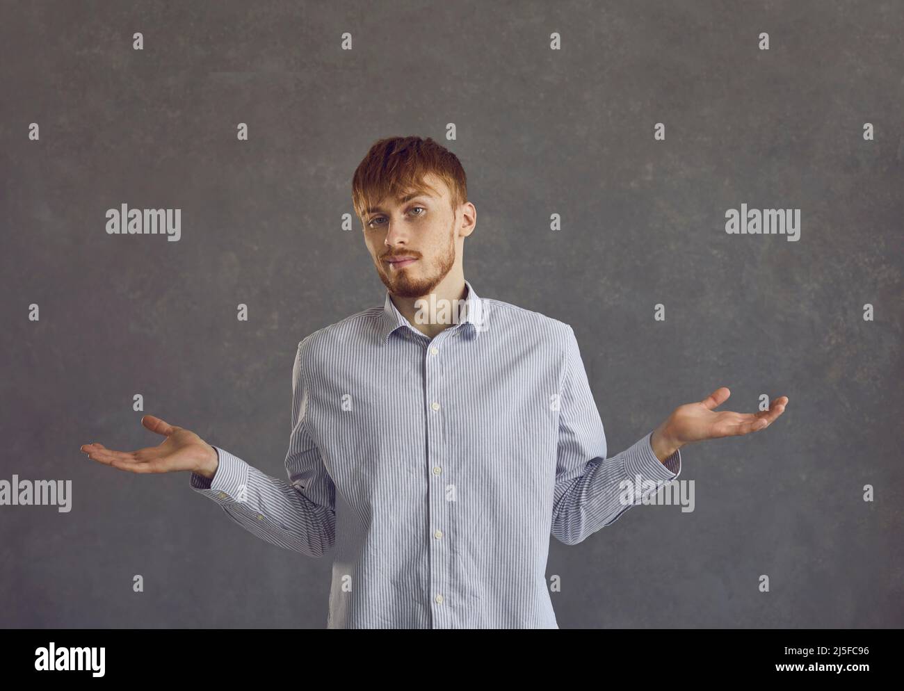 Giovane uomo arrogante in piedi su uno sfondo grigio timoroso e mostra un gesto di incertezza. Foto Stock