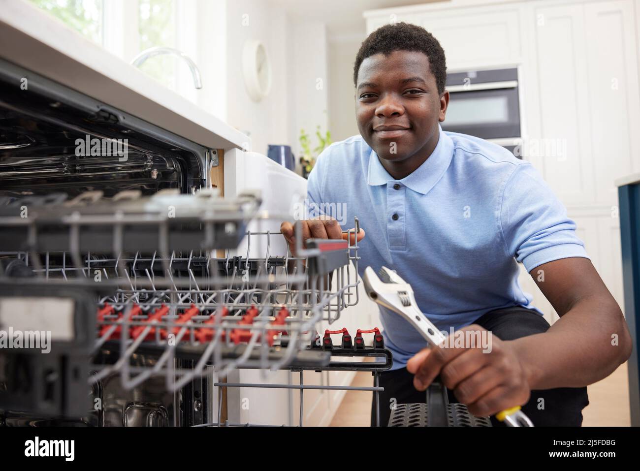 Ritratto di giovane formazione come idraulico fissando lavastoviglie domestica in cucina Foto Stock