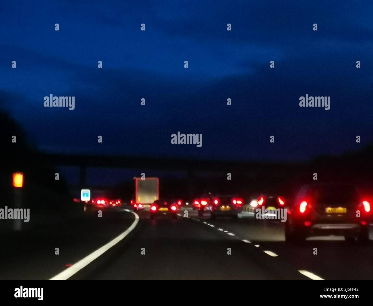 Luci auto posteriori sfocate in autostrada con cielo blu scuro sopra. Foto Stock