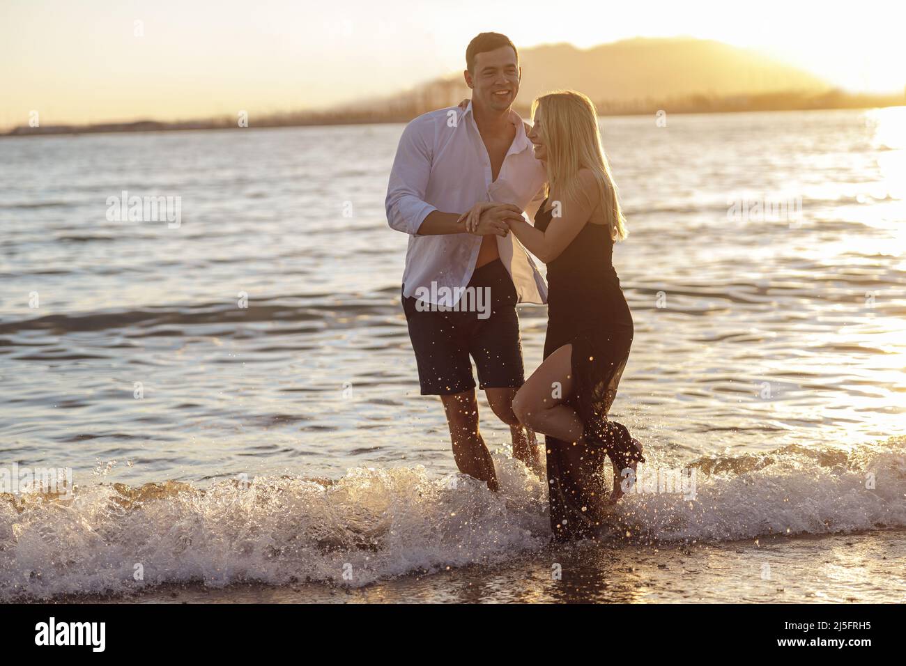 Tutta la lunghezza di bella coppia divertirsi mentre si cammina a piedi nudi lungo la spiaggia di sabbia Foto Stock