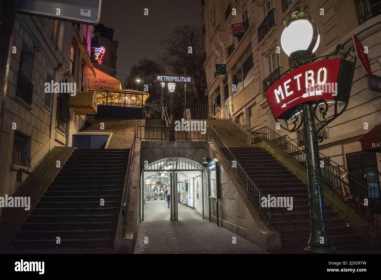 Parigi, Francia: Vista notturna, lampioni di strada e segni al neon all'ingresso della stazione della metropolitana di Montmartre, famosa collina nel nord 18th ° arrondissement Foto Stock