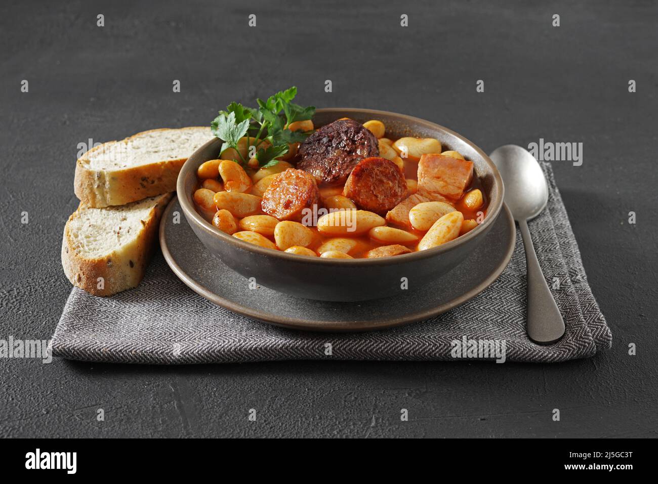Ricetta tradizionale di fagioli con chorizo e salsiccia di sangue di Fabada Asturiana su un tavolo scuro. Fuoco selettivo Foto Stock