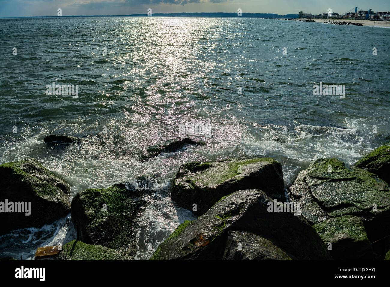 Onde che si infrangono sulle pietre in spiaggia Foto Stock