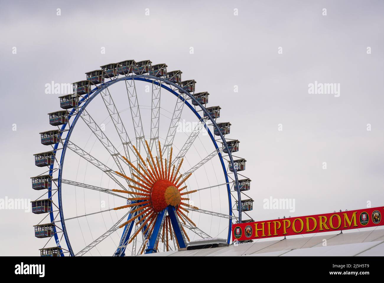 Bellissimo scatto di una zona fieristica con ruota panoramica e un cartellone per la tenda da birra Hippodrom al Festival di primavera di Monaco del 2022 sul Theresienwiese. Foto Stock