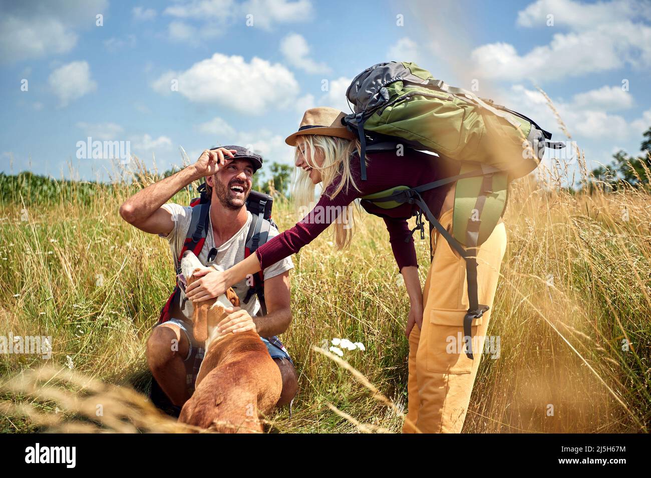 Una giovane coppia è di buon umore mentre si cammina un prato in una bella giornata di sole con il loro cane. Escursioni, natura, relazione, insieme Foto Stock