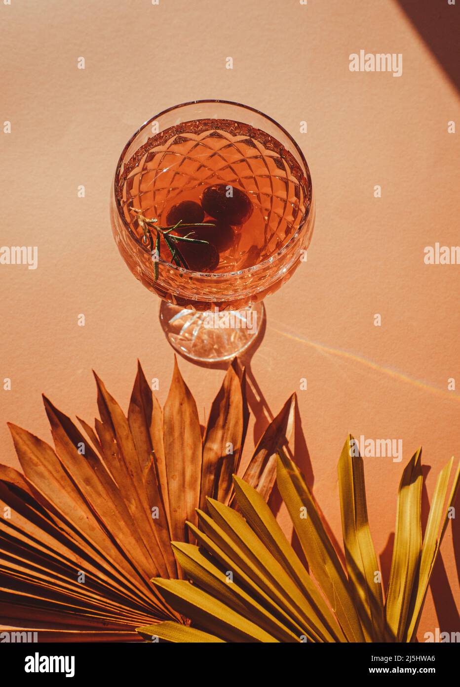 Vino spritzer o gin tonico con uva e ramoscello rosmarino, un gustoso cocktail estivo isolato su sfondo beige boho con foglie di palma secche Foto Stock