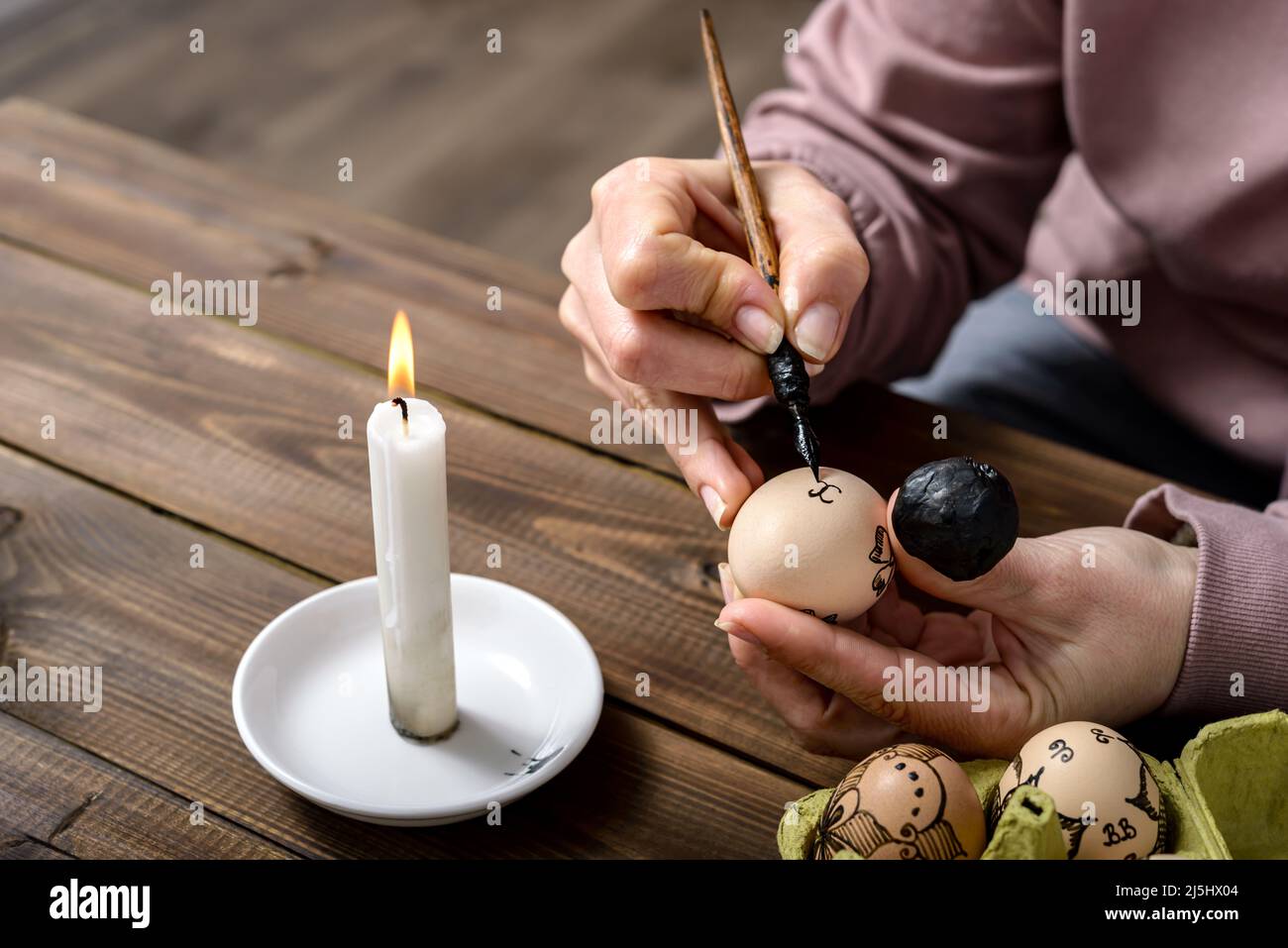 Le mani femminili tradizionalmente dipingono le uova con i modelli floreali usando una penna della fontana e la cera per Pasqua sul tavolo di legno. Concetto di preparazione pasquale. Foto Stock