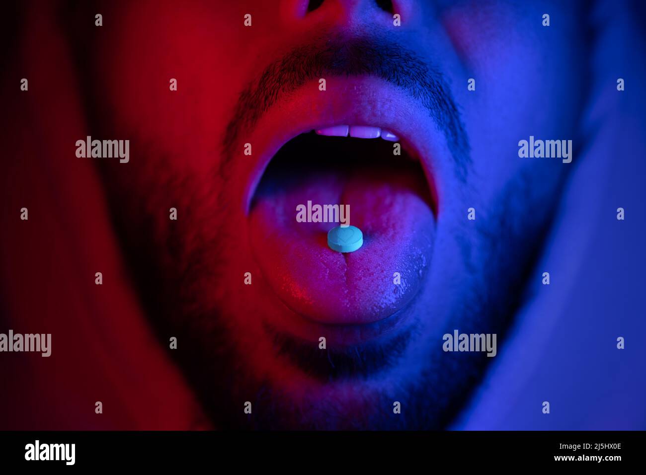 Primo piano della bocca dell'uomo inghiottendo i farmaci estasi. Uomo che prende MDMA pillola ecstasy. Foto Stock