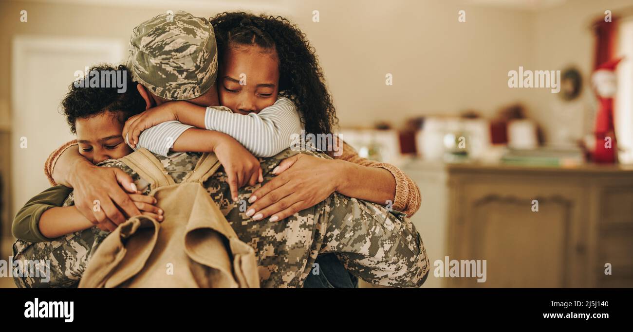 Soldato che abbraccia sua moglie e i suoi figli nel suo ritorno a casa. Il serviceman riceve un caloroso benvenuto dalla sua famiglia dopo il ritorno dall'implementazione. Militare f Foto Stock