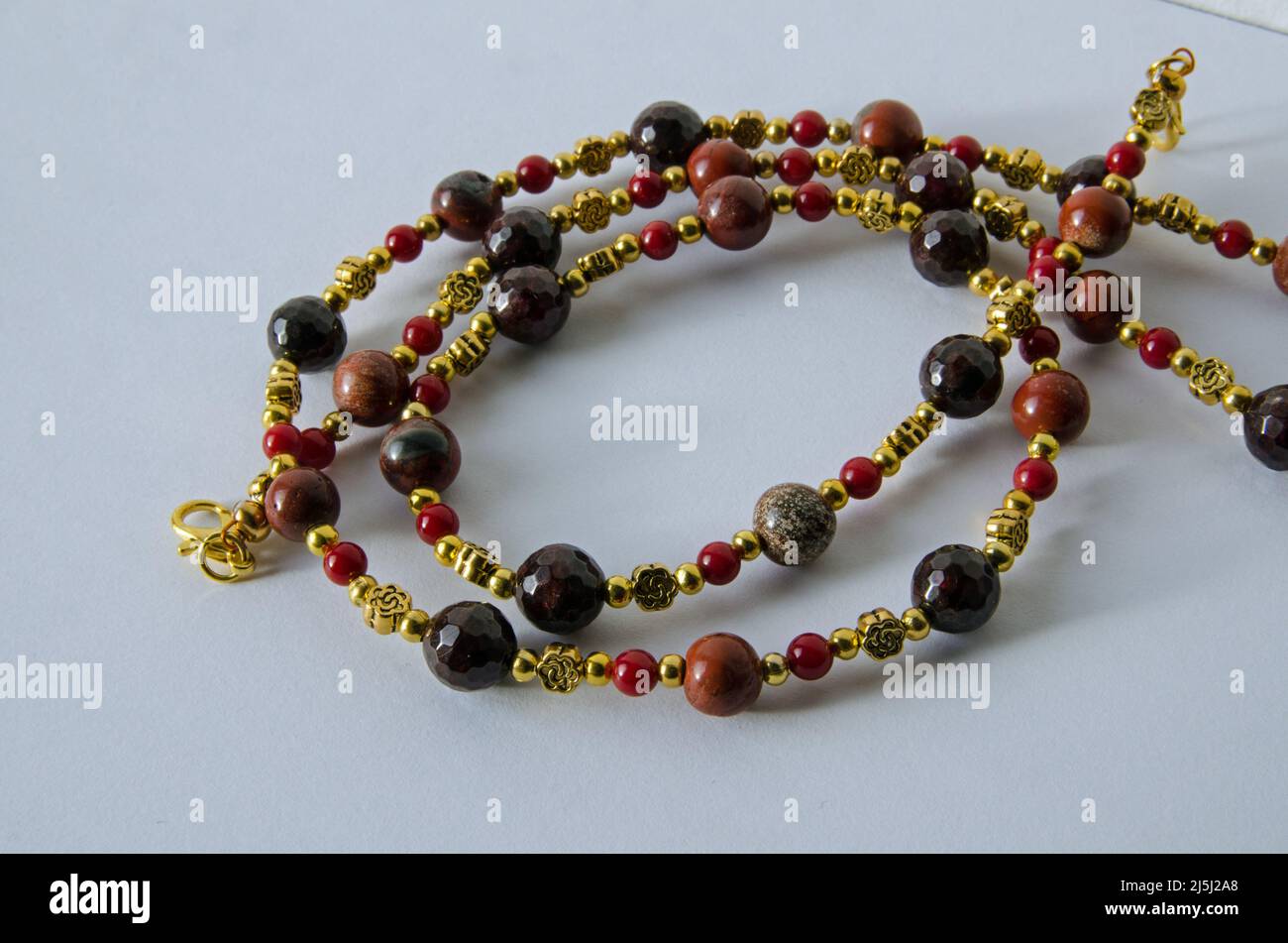 Collana fatta a mano da perle di granato, diaspro e corallo con reperti dorati su sfondo bianco. Foto Stock