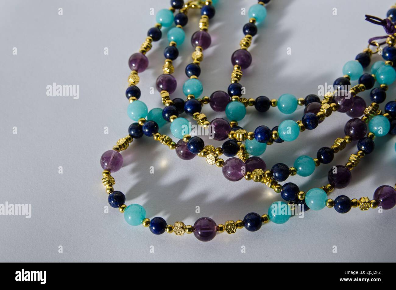 Spirali di una collana fatte a mano da perle di ametista viola, lapislazzuli blu e pietre quarzite turchesi. Vista su sfondo bianco con dr Foto Stock