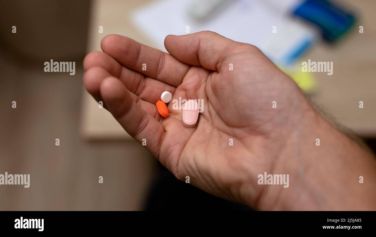 mano dell'uomo che tiene parecchie pillole nella sua mano sullo sfondo domestico di sfocatura. Medicina e concetto di assistenza sanitaria. Foto Stock