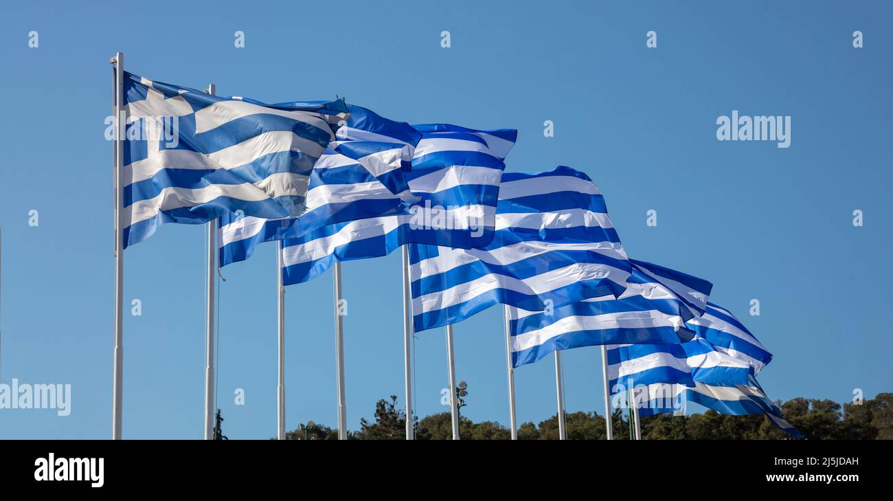 Bandiere ufficiali nazionali greche sui flagpoli in fila che ondeggiano nel vento. Simbolo di segno della Grecia, cielo azzurro chiaro, giorno di primavera soleggiato ad Atene. Foto Stock