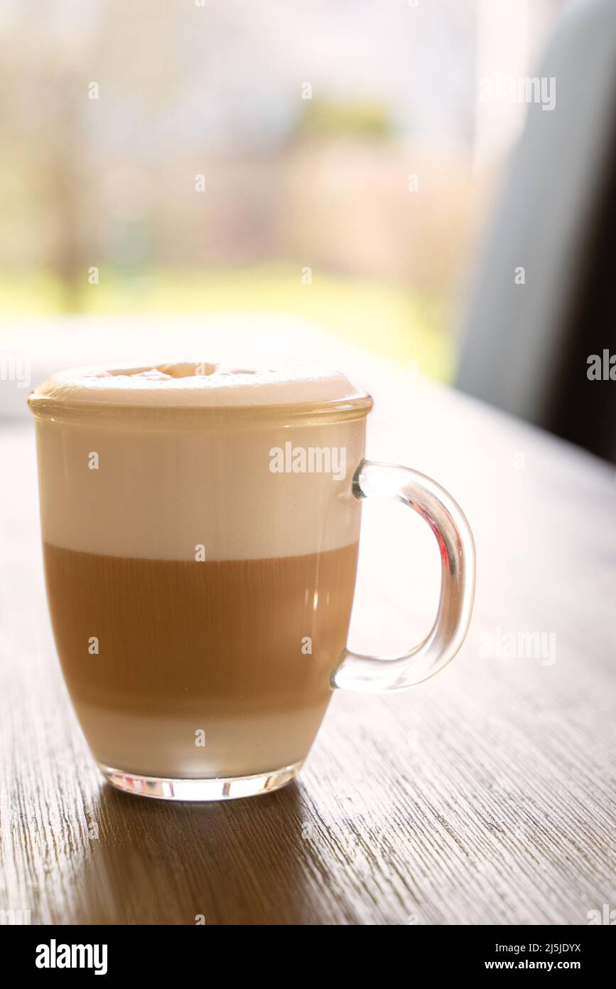 Latte macchiato appena fatto su un tavolo di legno in una tazza di caffè di  vetro con finestra che conduce al giardino sullo sfondo Foto stock - Alamy