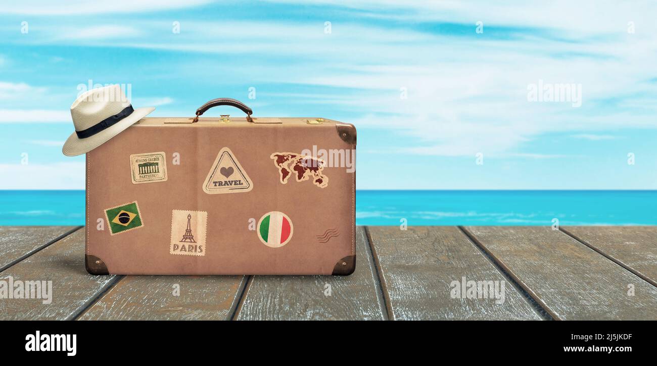 Vecchia valigia da viaggio e cappello bianco su pavimento in legno con mare e cielo sullo sfondo. Spazio di copia accanto. Concetto di viaggio tropicale. Foto Stock