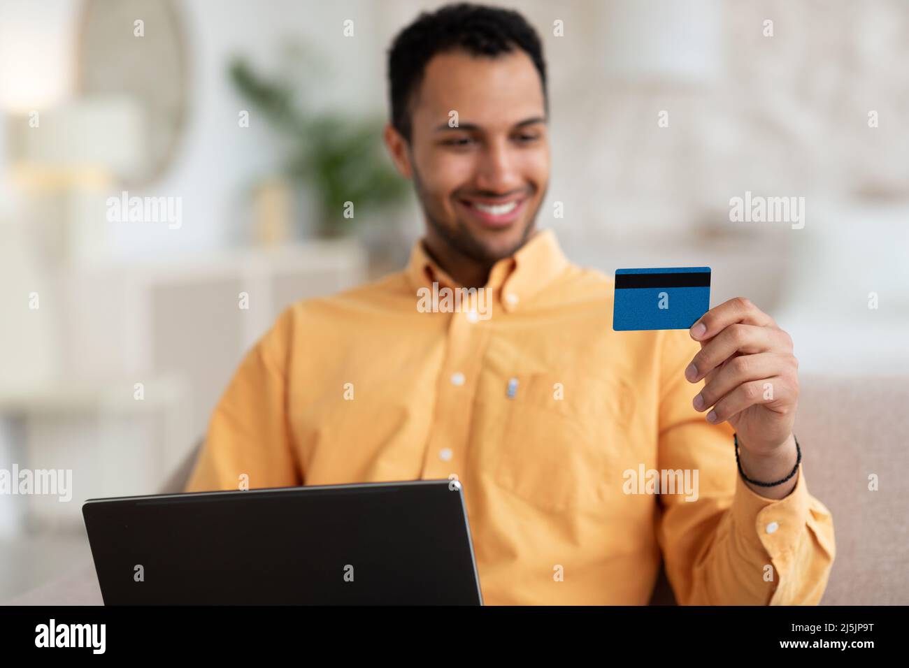Uomo sorridente che usa il pc e la carta di credito a casa Foto Stock