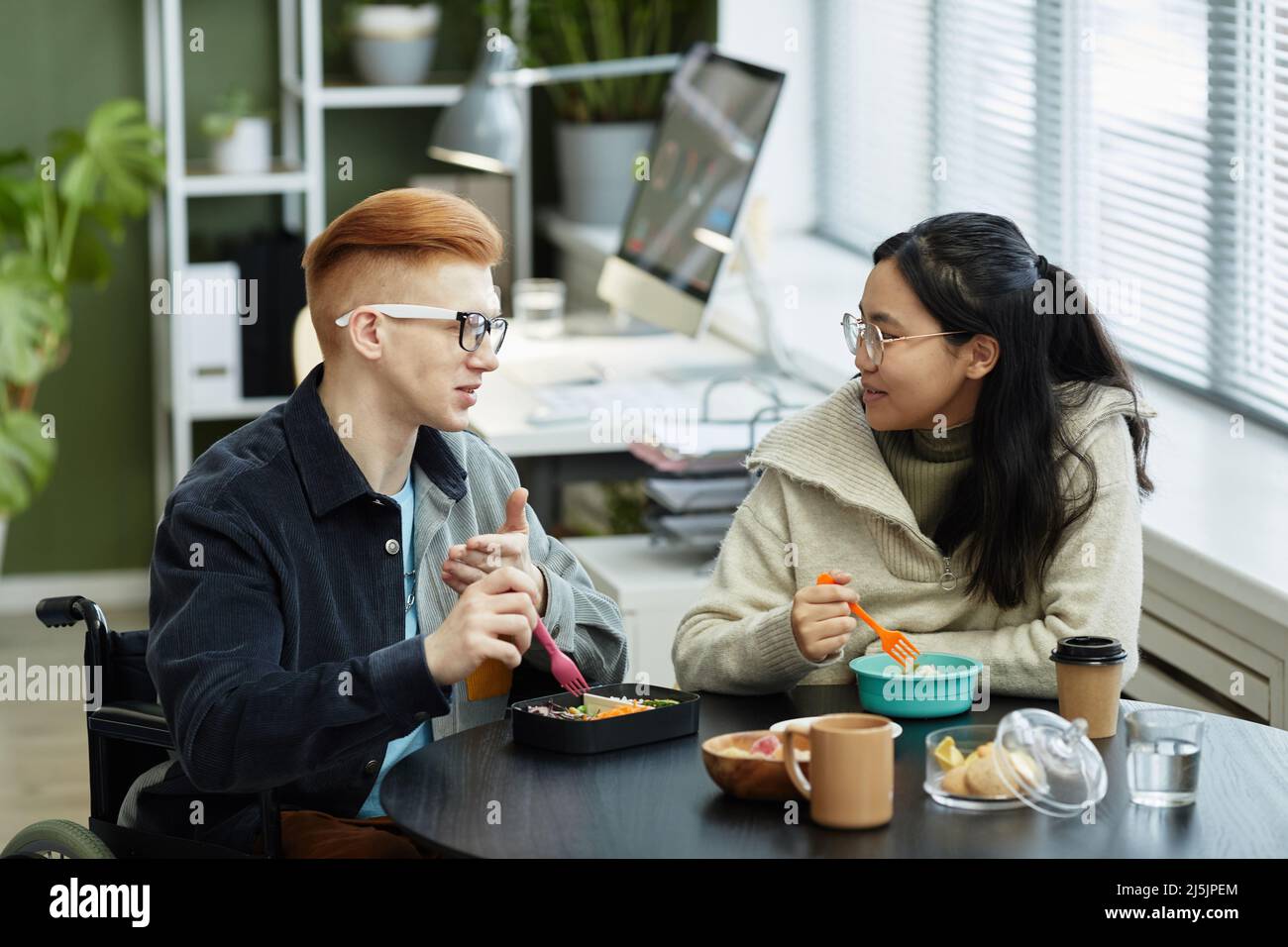 Ritratto laterale di due giovani sorridenti che mangiano il pranzo al lavoro e si divertono a conversare Foto Stock