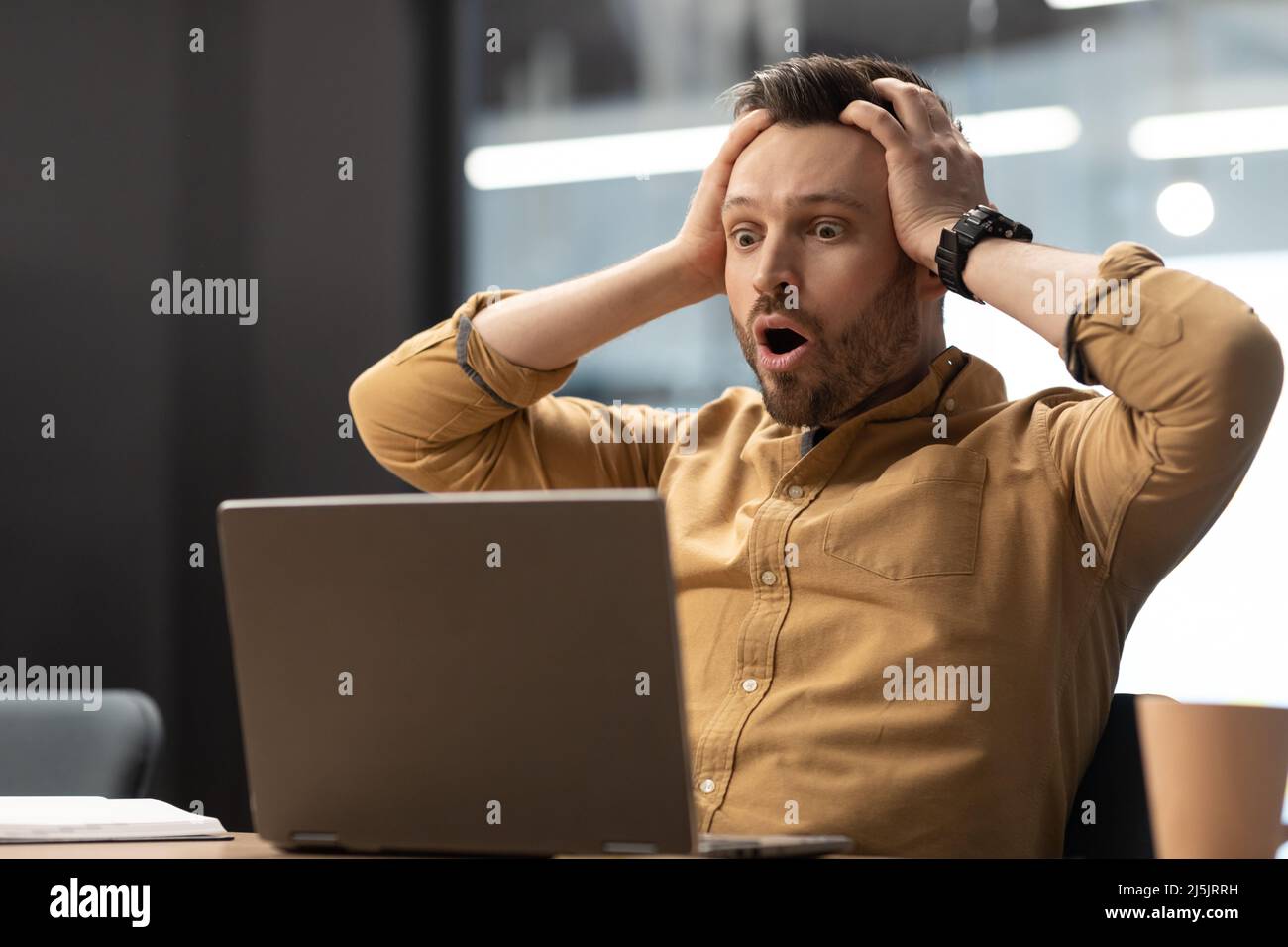 Uomo d'affari che tocca la testa guardando il notebook in shock in ufficio Foto Stock
