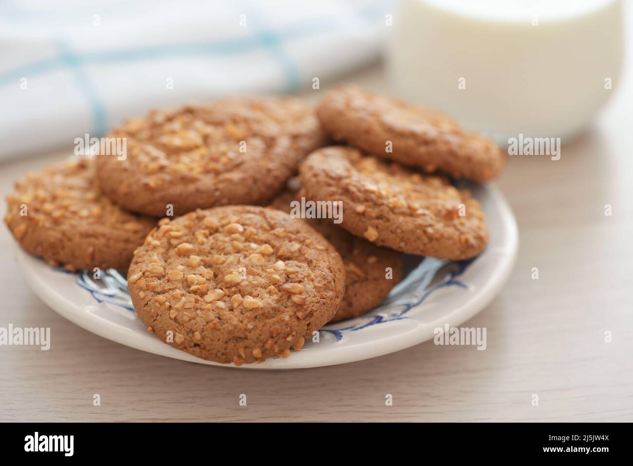 Primo piano di biscotti di farina d'avena con briciole di arachidi e un bicchiere di latte su un tavolo di legno Foto Stock