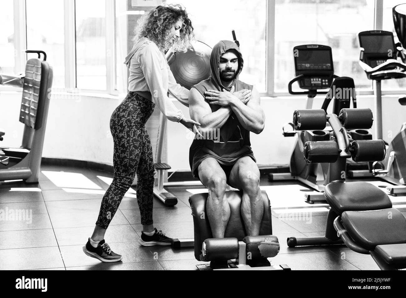 Giovane uomo adulto che si sta allenando in palestra - fare esercizi alle gambe con l'aiuto del suo personal trainer Foto Stock