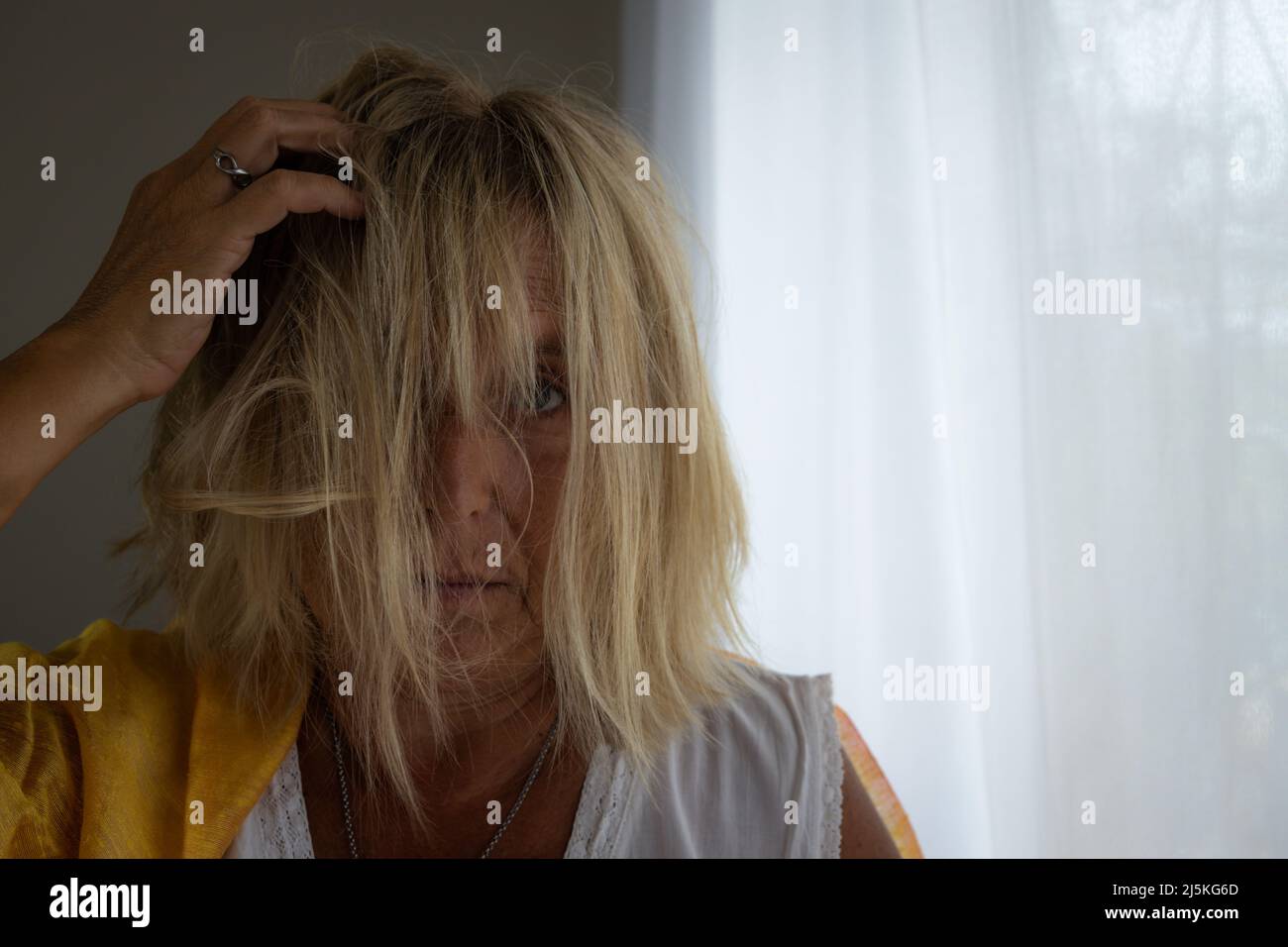 Donna caucasica bionda di 50-60 anni con capelli tosati su sfondo neutro. Concetto di donna stressato. Foto Stock