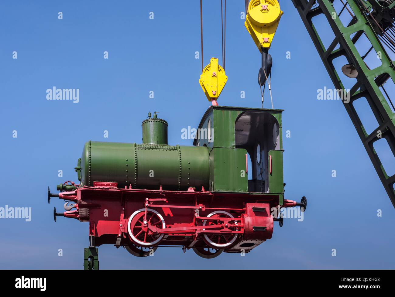 Carino trenino verde nostalgico a vapore appeso in aria su un camion gru, blu skye e spazio copia, Germania Foto Stock