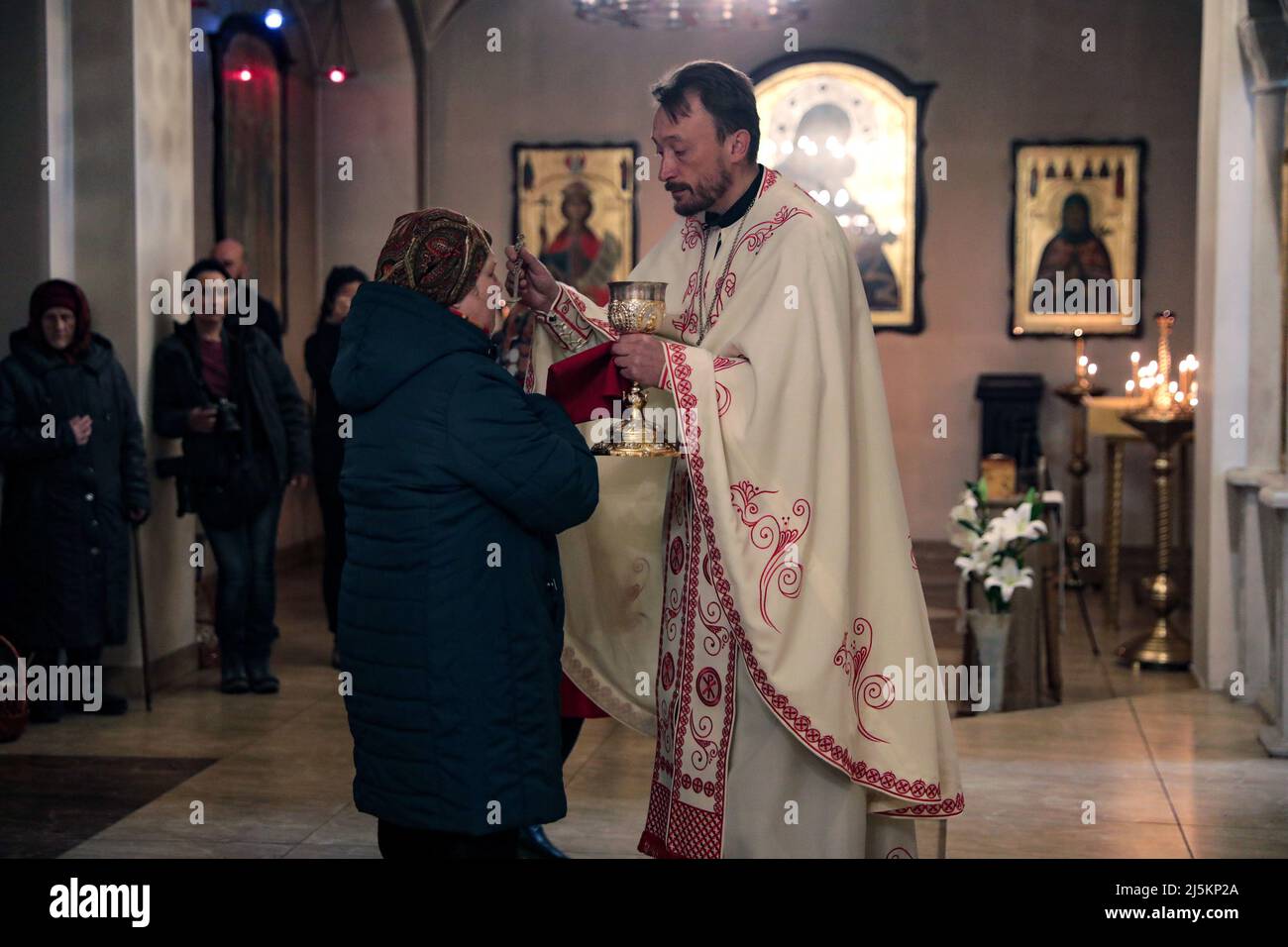 BUCHA, UCRAINA - APRILE 24, 2022 - Un sacerdote offre la comunione ad una donna durante una liturgia pasquale nella Chiesa di Sant'Andrea il primo apostolo chiamato durante la celebrazione della Pasqua Ortodossa a Buca che si sta riprendendo dai crimini di guerra commessi dalle truppe russe dopo la sua liberazione dagli invasori russi, nella Regione di Kyiv, nel nord dell'Ucraina. Credit: Ukrinform/Alamy Live News Foto Stock