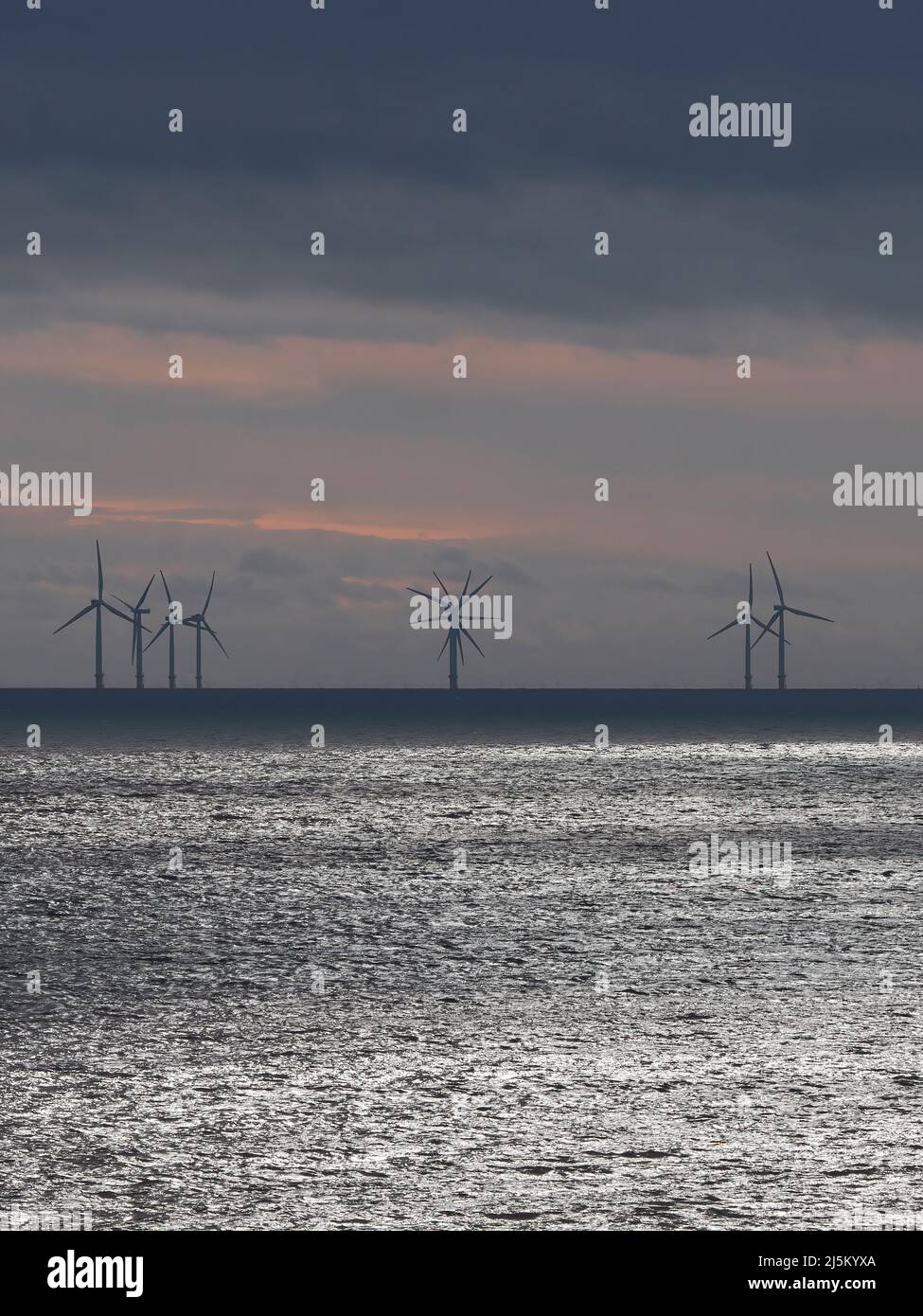 Le turbine a silhouette di un parco eolico si innalzano all'orizzonte nel Mare del Nord sotto un cielo drammatico e tempestoso. Foto Stock