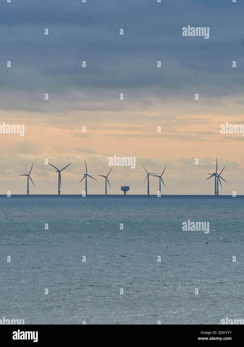 Le turbine a silhouette di un parco eolico, sorvegliate dall'orlo di un forte di Maunsell, si ergono all'orizzonte nel Mare del Nord sotto un cielo drammatico e tempestoso. Foto Stock