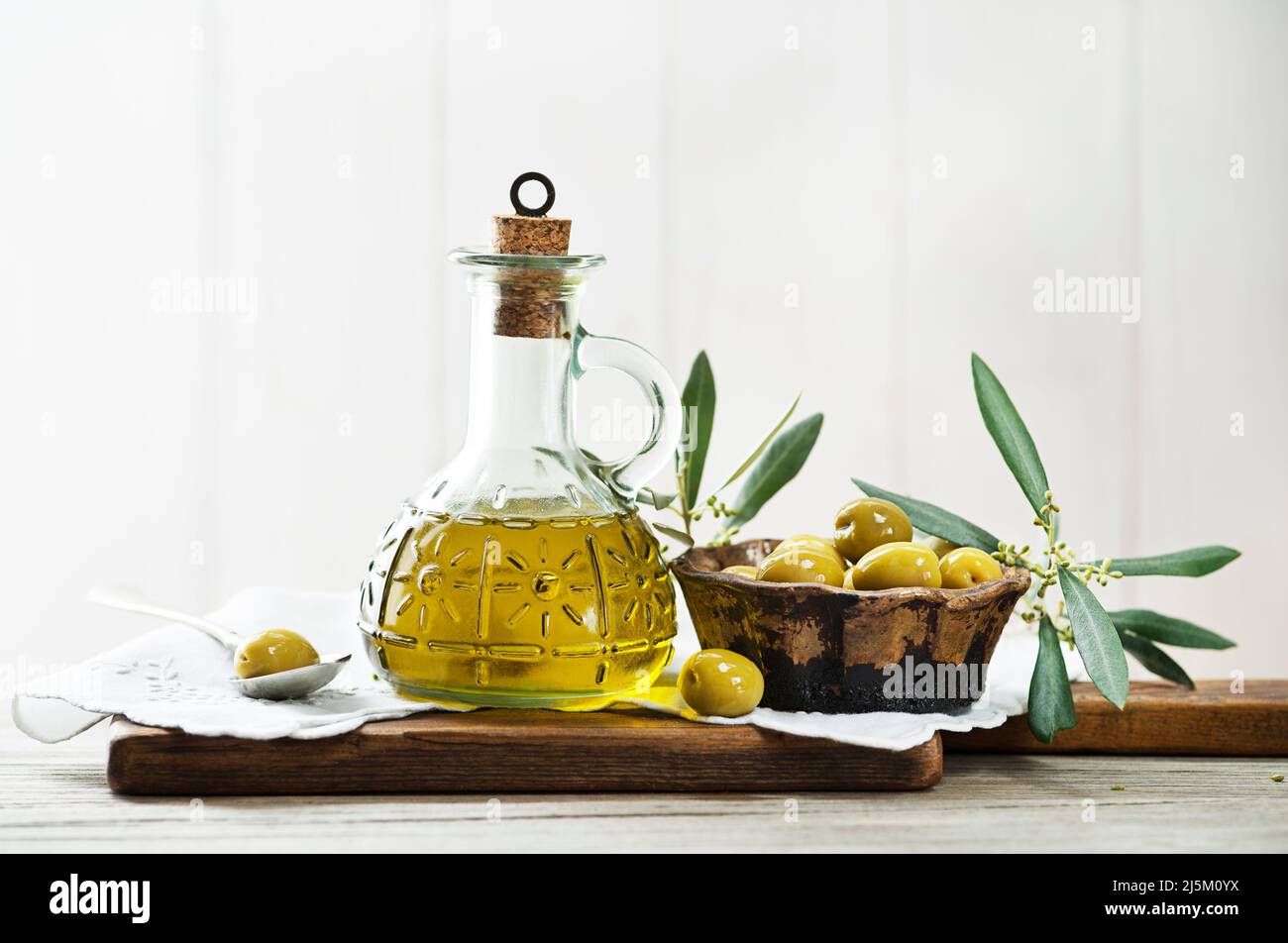 Bottiglia d'olio d'oliva e ramo d'oliva con olive verdi sott'aceto su tavola di legno Foto Stock