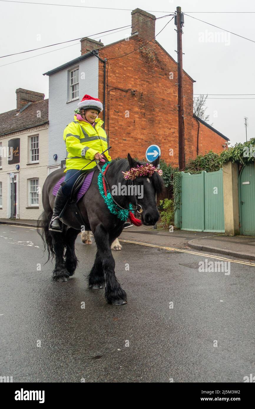 Femmina che indossa un cappello di Natale a cavallo nero vestito in tinsel lungo una strada nel centro di Newport Pagnell, Buckinghamshire, Engla Foto Stock