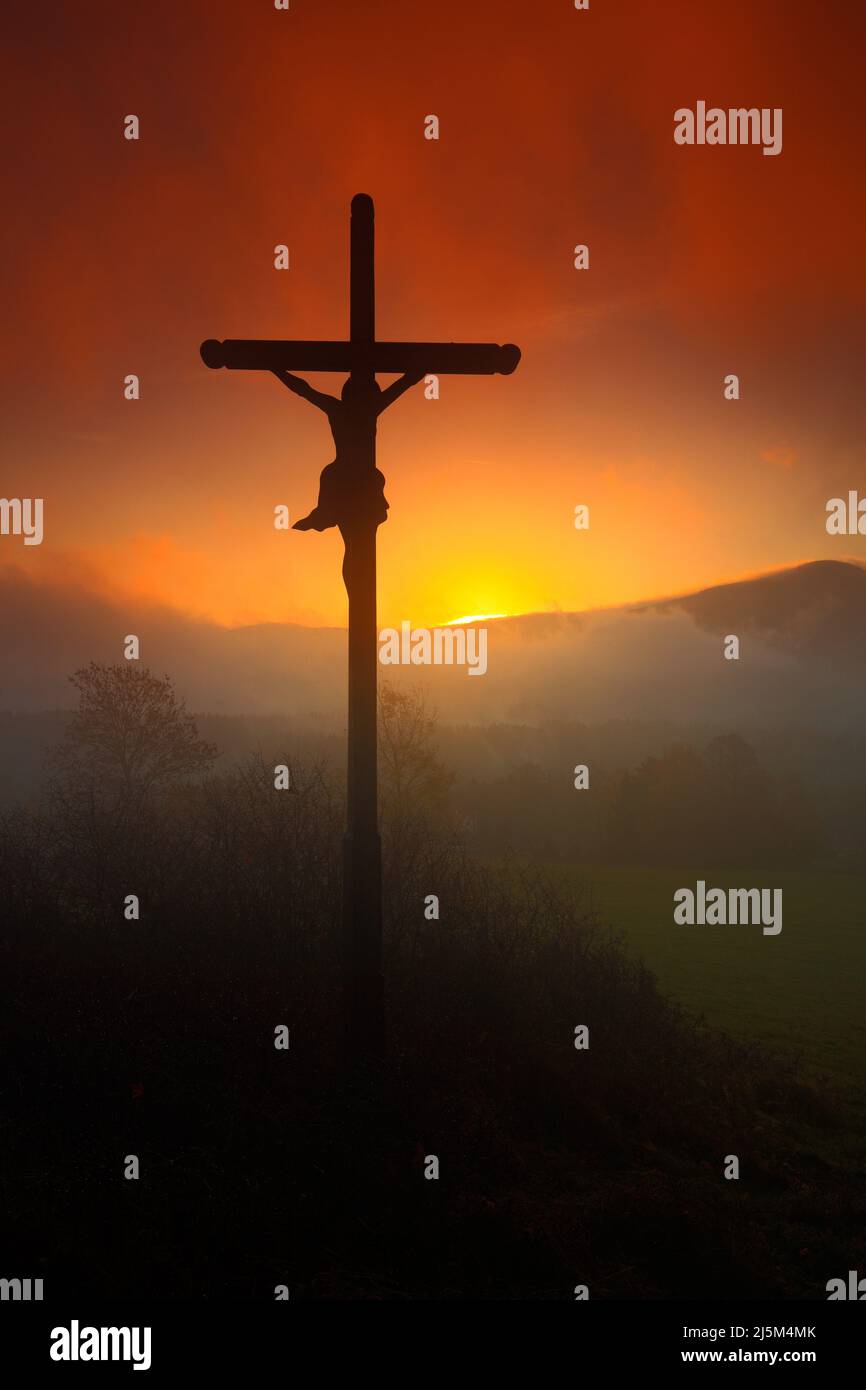 Attraversa il bellissimo tramonto con la nebbia. Paesaggio ceco con croce con sole arancione e nuvole al mattino. Paesaggio mistico collinare con croce. Fine di Foto Stock