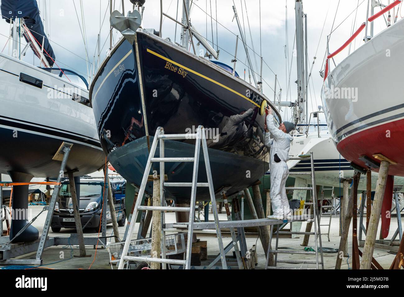 Tecnico maschile che lavora duro lucidando lo scafo di uno yacht in stoccaggio a secco nella stagione invernale per le attività di manutenzione, Hamble Point Marina Inghilterra UK Foto Stock