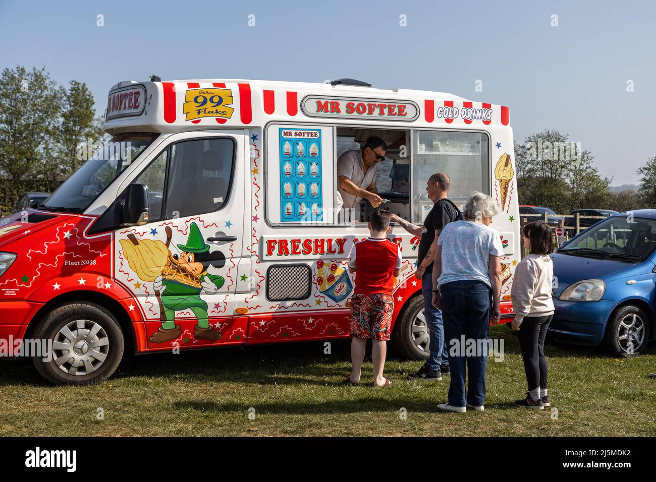 Un venditore di gelati serve dal suo furgone con clienti desiderosi in attesa in fila Foto Stock